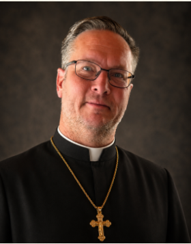 Rev. Fr. Christopher Nerreau in a black cassock with a gold pectoral cross
