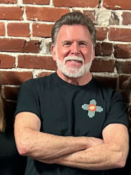 Mark McGrail, the parish musician, smiling with his arms crossed in front of an exposed brick wall.