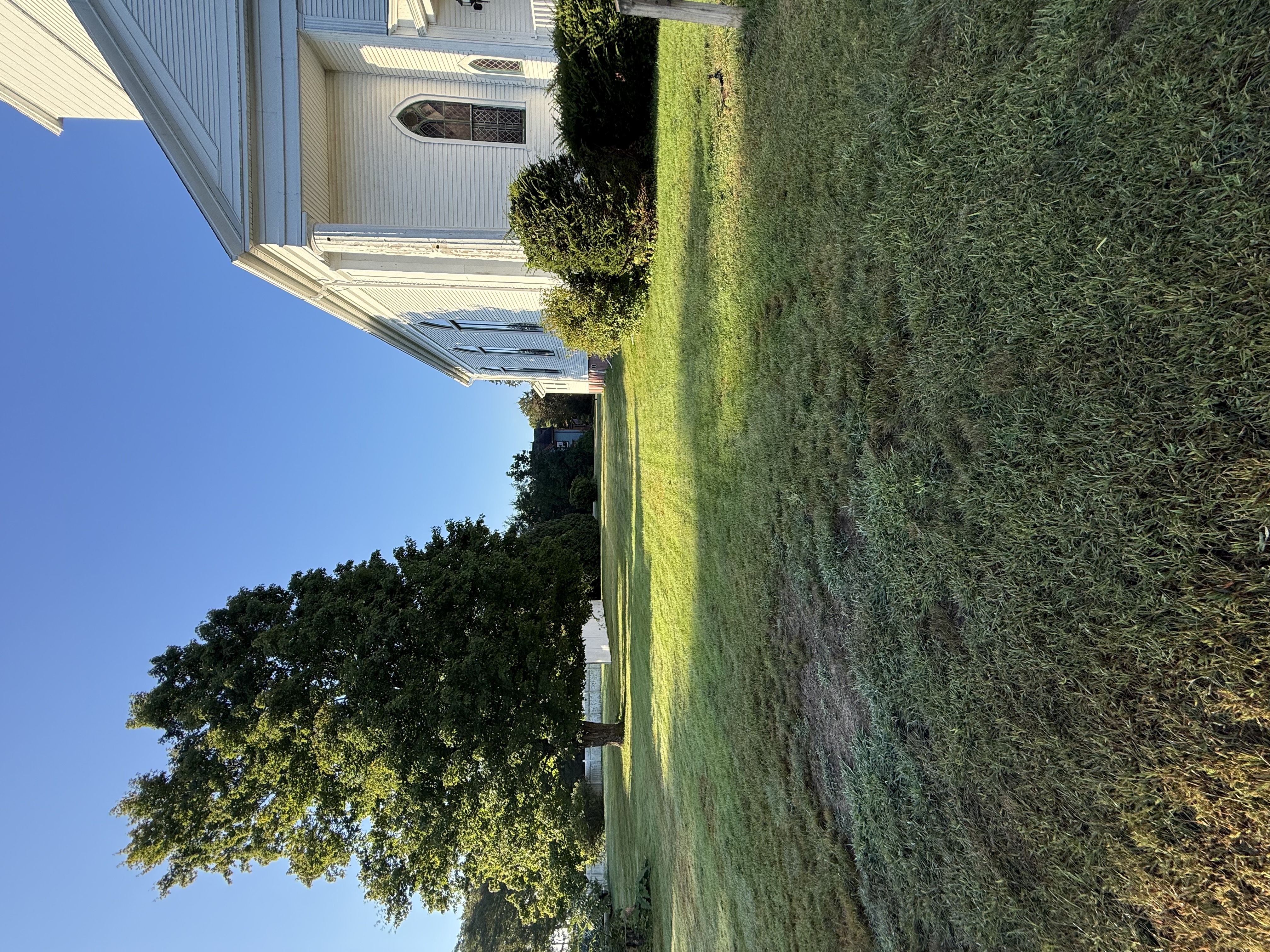 Side of the white church with its tall arched windows beside a large tree on the lawn