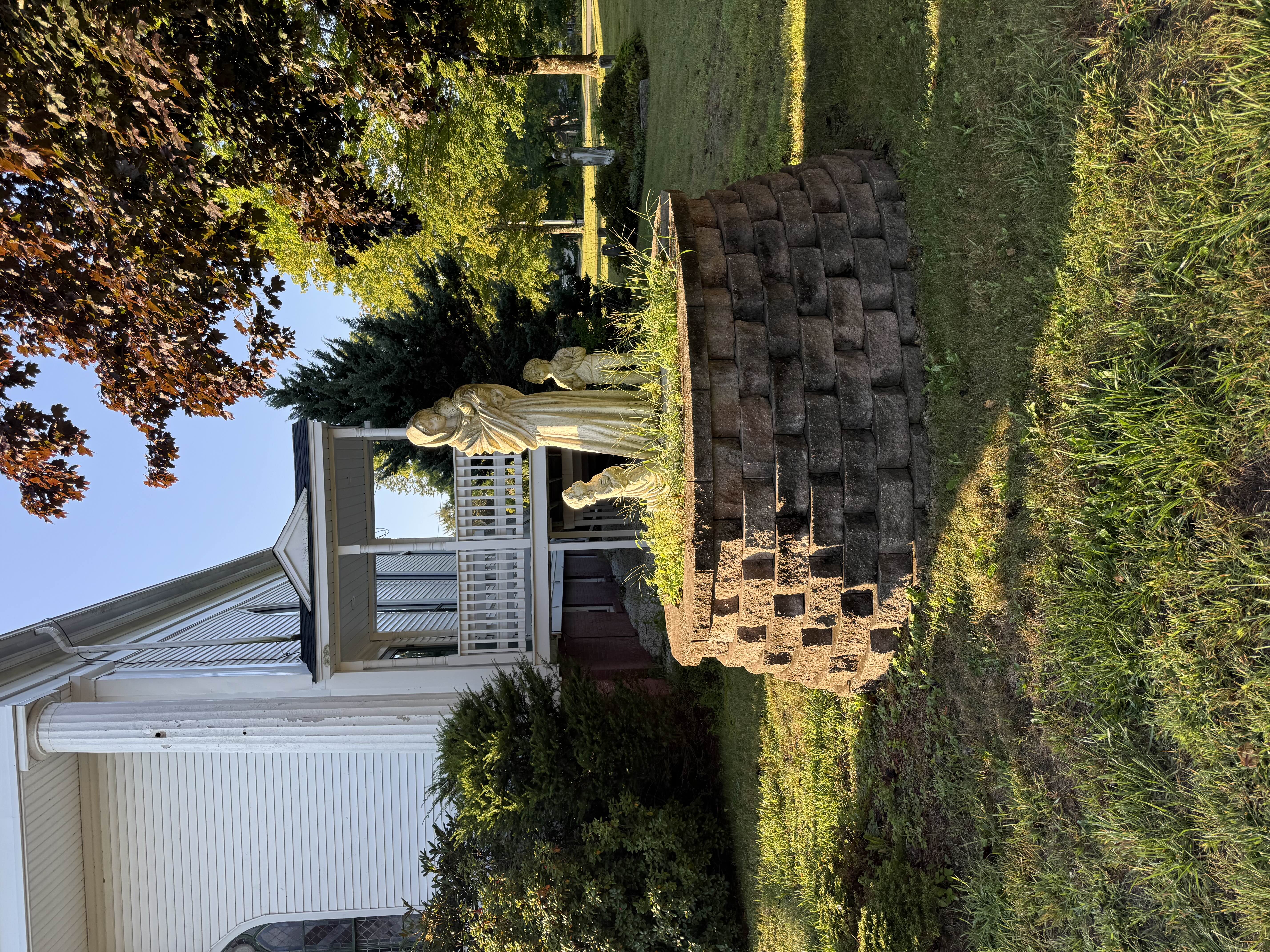 A statue of the Madonna and Child with two kneeling children set on a circular stone garden wall beside the church porch