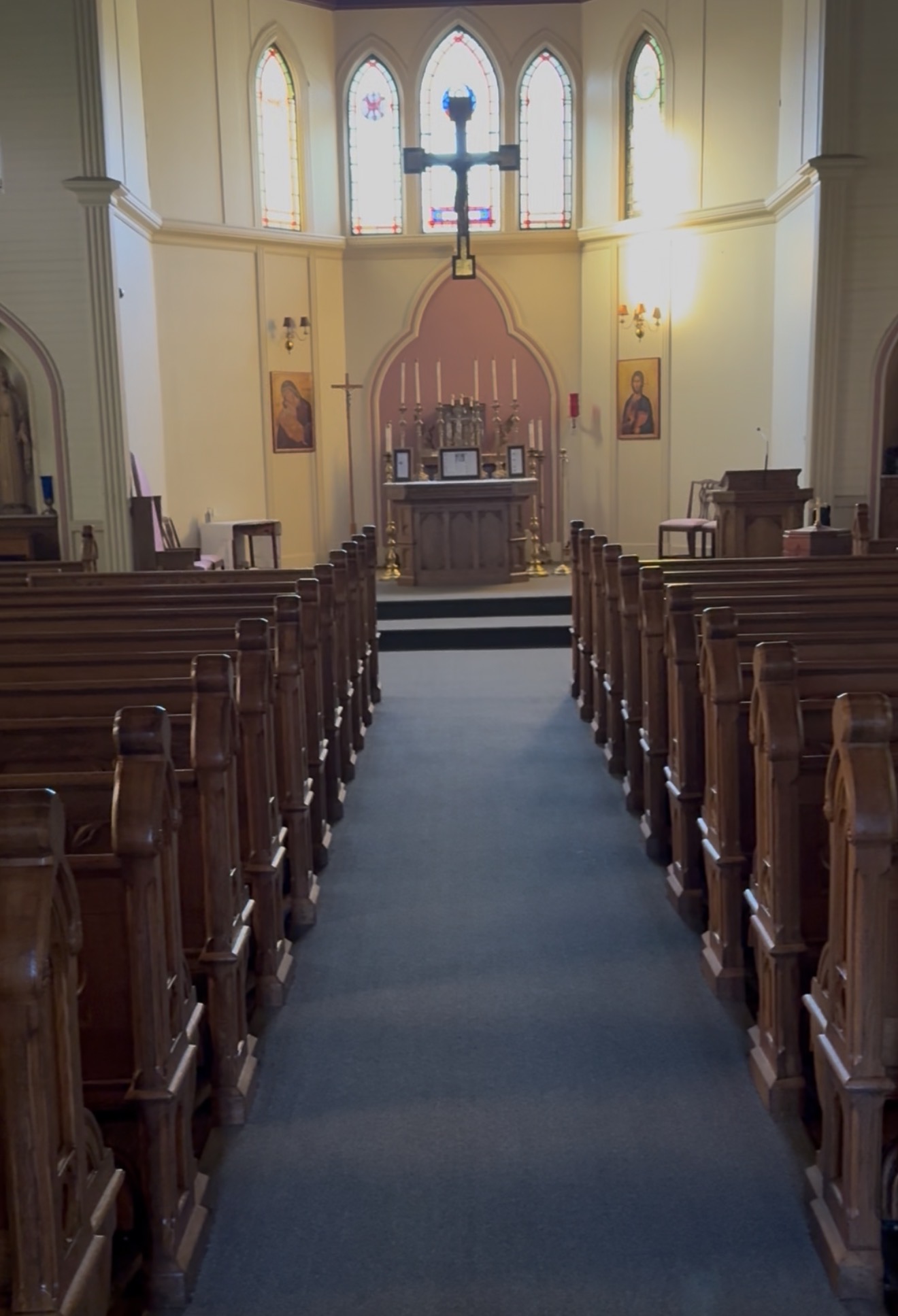 The nave looking down the center aisle toward the altar, crucifix, and stained glass, with icons of the Theotokos and Christ